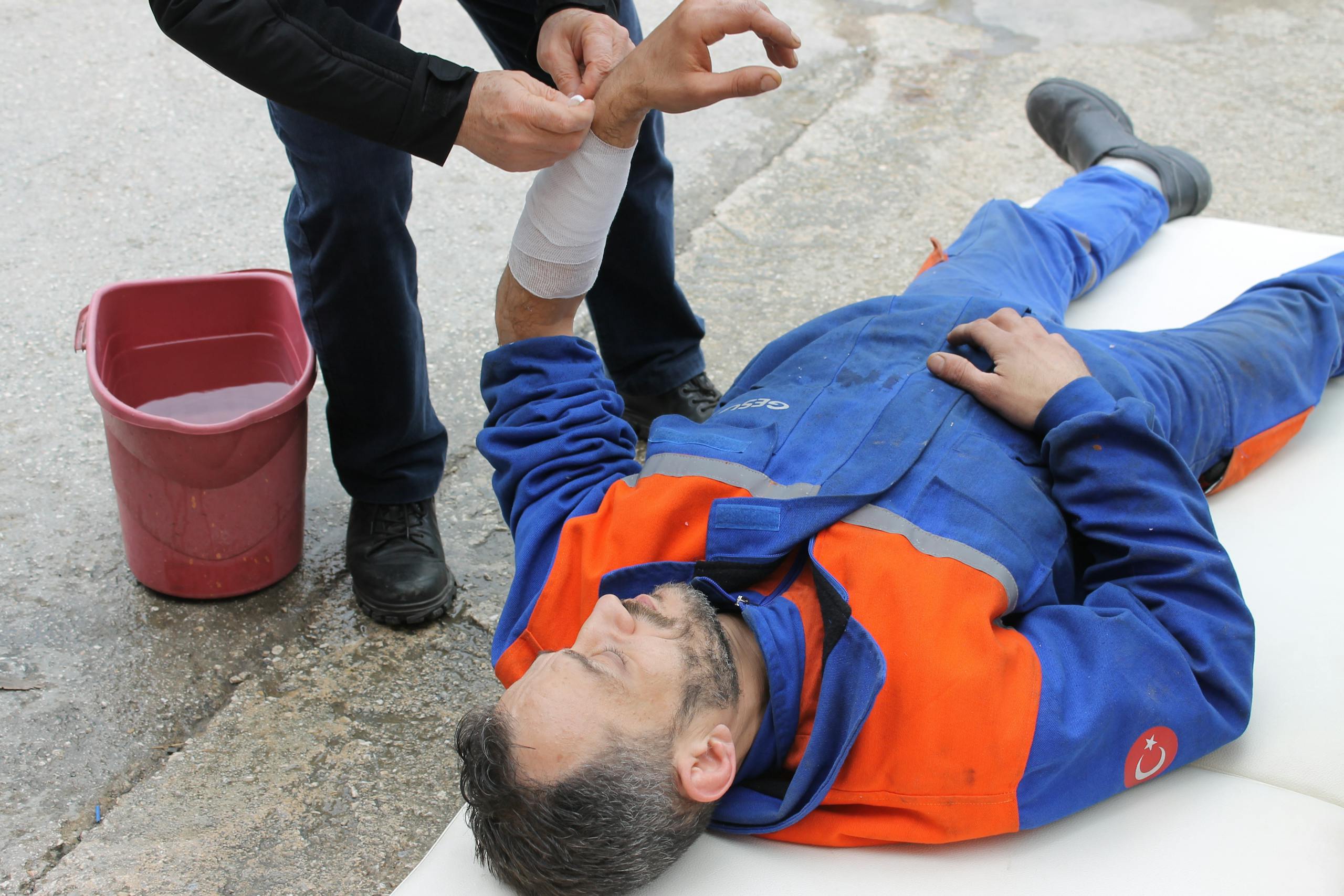 Injured worker receiving first aid on-site with arm bandage applied.