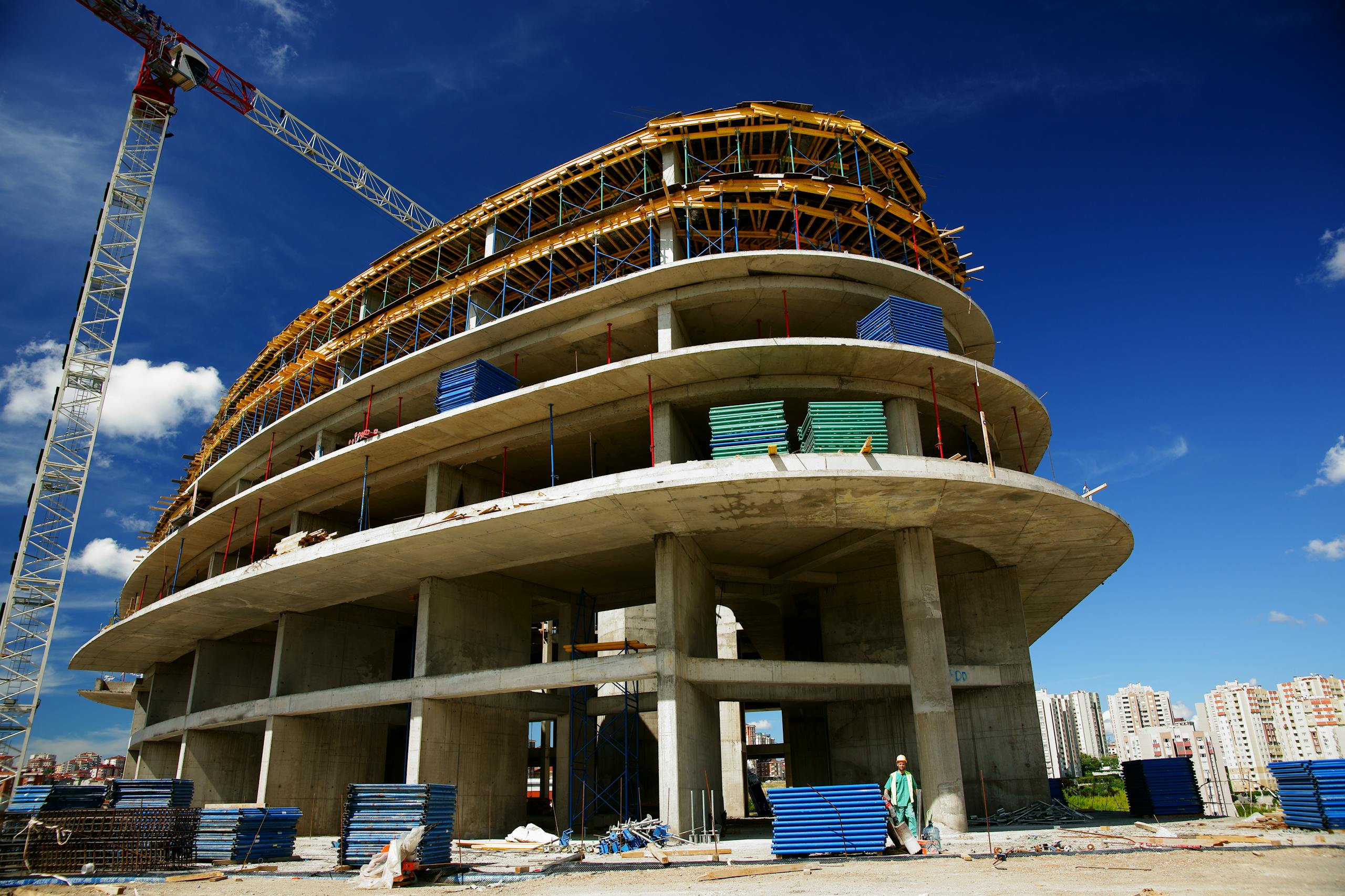 Low angle view of a circular building under construction with a crane, clear blue sky.