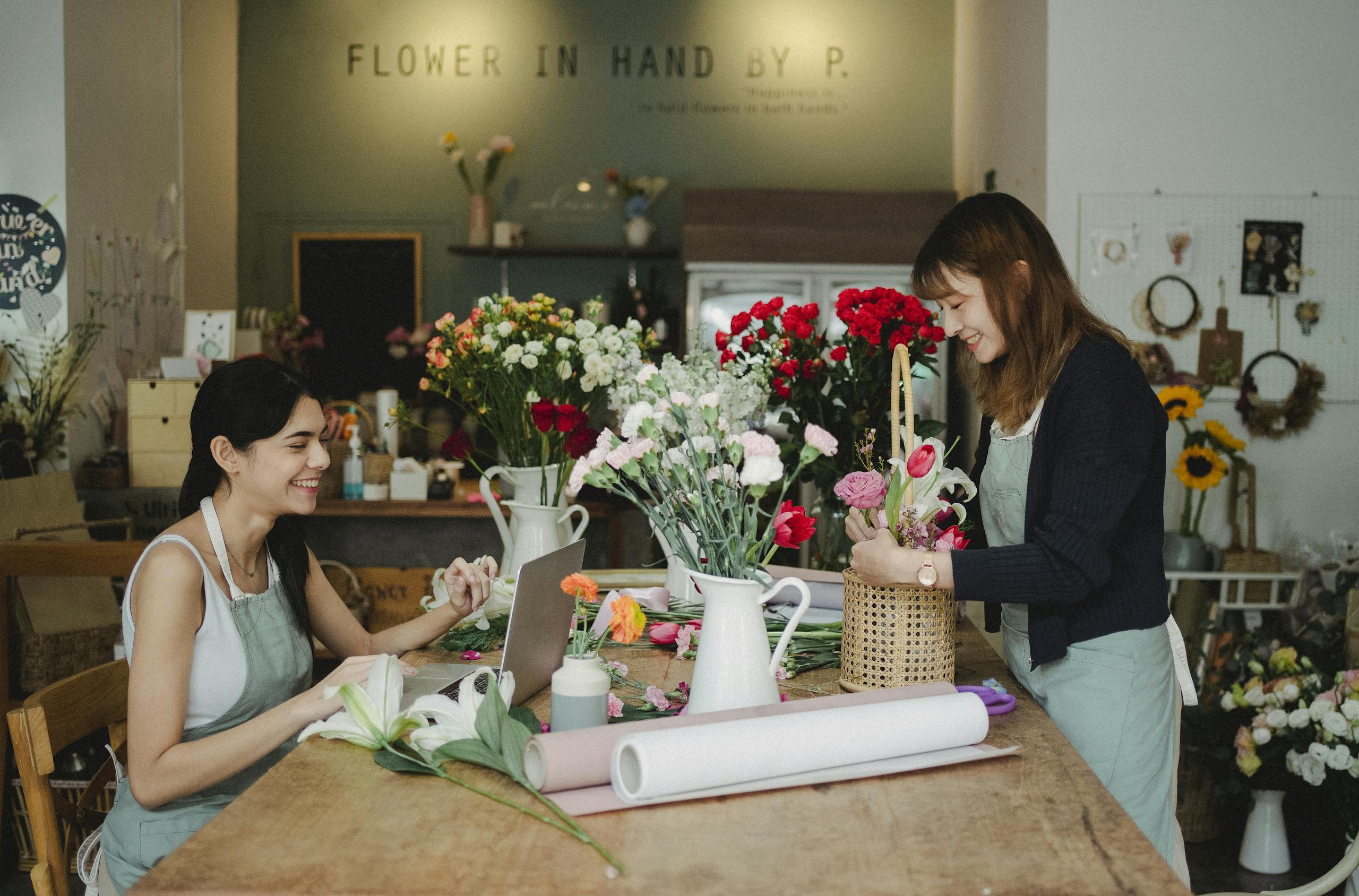 Two women florists happily arranging flowers in a cozy flower shop workspace.